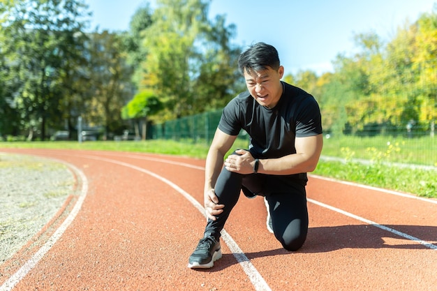 Un homme asiatique après une séance d'entraînement physique et un jogging est assis sur le sol et souffre de massages de la douleur des jambes