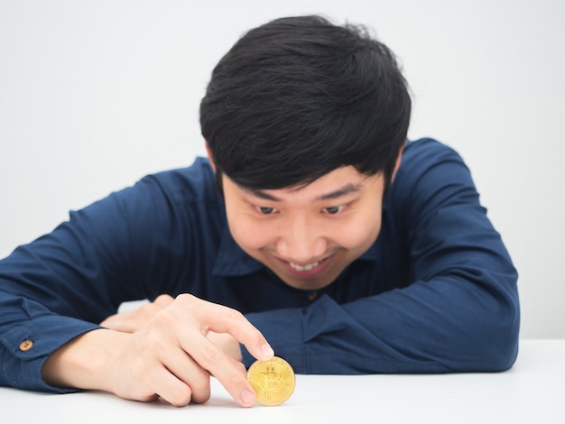 Homme asiatique assis au bureau et regardant le bitcoin doré à la main avec le sourire