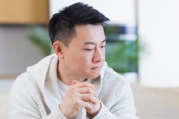 homme asiatique assis sur un canapé à la maison pensif inquiet des problèmes et de la dépression