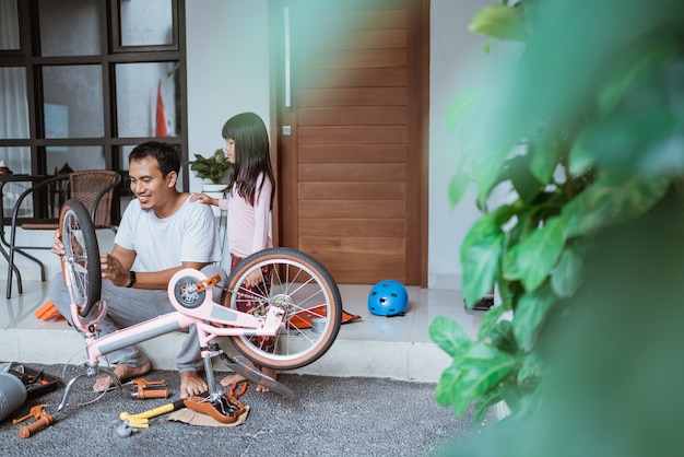 Homme asiatique assis tout en réparant un vélo avec une petite fille