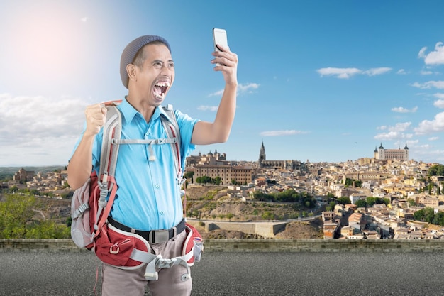 Homme asiatique avec un bonnet et un sac à dos prenant un autoportrait avec son téléphone dans la rue