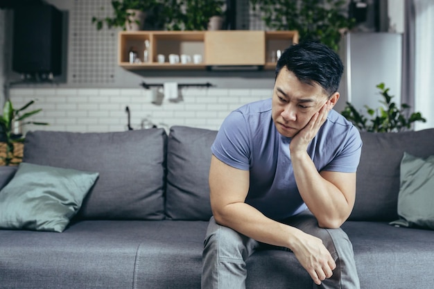 Homme asiatique bouleversé à la maison fatigué et déprimé assis sur le canapé dans le salon