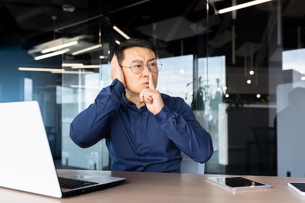 Homme asiatique bouleversé et nerveux sur le lieu de travail exigeant le silence de ses collègues homme d'affaires tenant