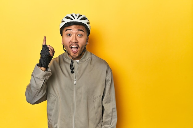 Un homme asiatique avec un casque de vélo et des gants, une toile de fond de studio jaune, ayant une idée, un concept d'inspiration.