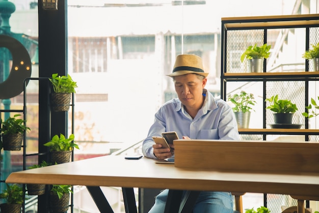 Homme asiatique en chemise décontractée tient deux téléphones mobiles et confondu sur une table en bois au café