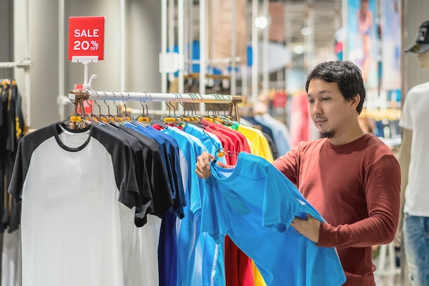 Homme asiatique chic avec barbe en choisissant des vêtements dans un magasin de vêtements au centre commercial