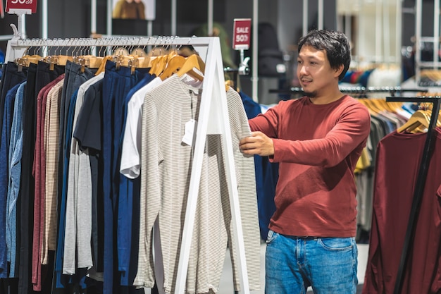 Homme asiatique chic avec barbe en choisissant des vêtements dans un magasin de vêtements au centre commercial