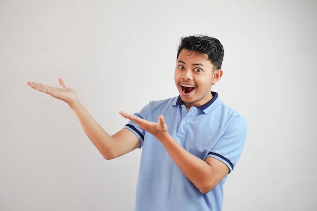 homme asiatique choqué avec une main ouverte avec les doigts pointant vers le côté portant un t-shirt bleu isolé
