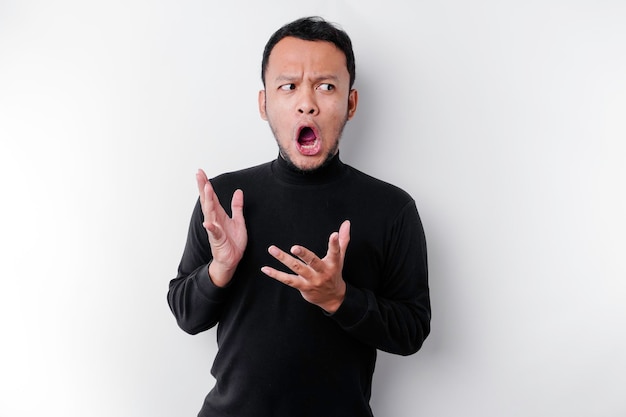 Homme asiatique choqué avec sa bouche grande ouverte portant une chemise noire isolée par un fond blanc