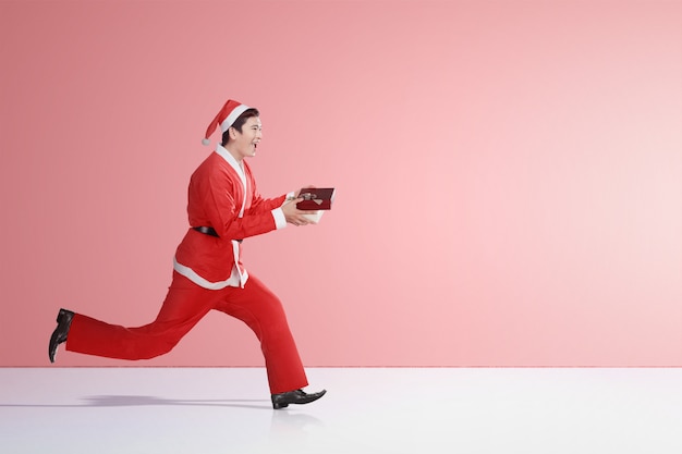 Homme asiatique en costume de père Noël en cours d'exécution tout en maintenant la boîte-cadeau