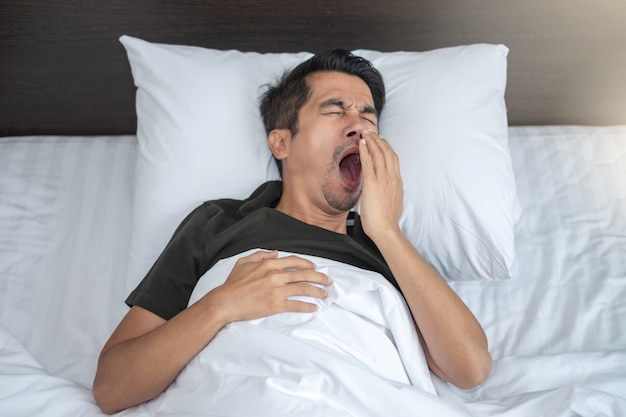 Homme asiatique couché bâillements et somnolent dans un lit blanc