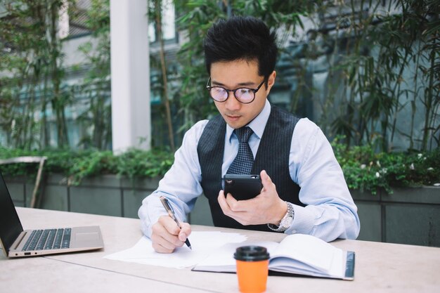 Homme asiatique en cravate et costume prenant des notes dans un cahier