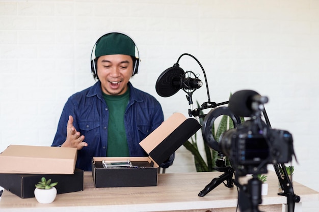 Homme asiatique dans un style décontracté déballant et examinant le produit à l'aide d'un équipement de podcast professionnel.