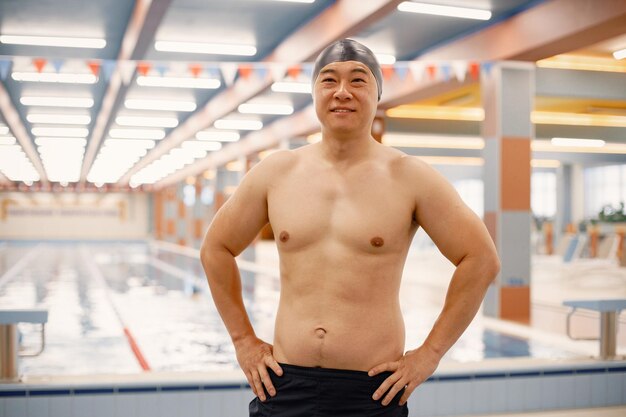 Homme asiatique debout dans une piscine intérieure et portant un chapeau