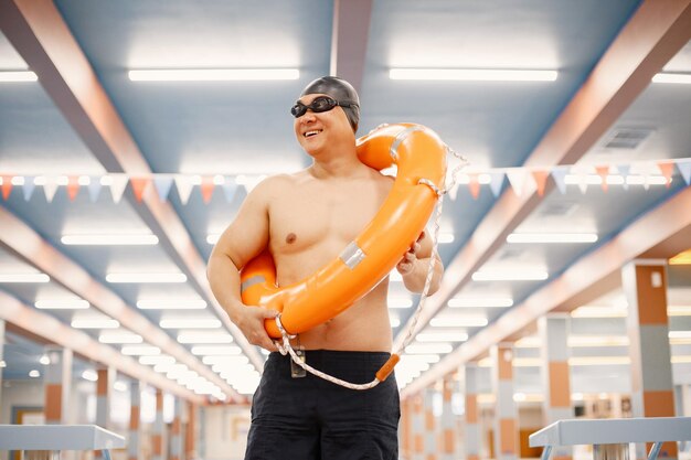 Homme asiatique debout dans une piscine intérieure et tenant un cercle de natation