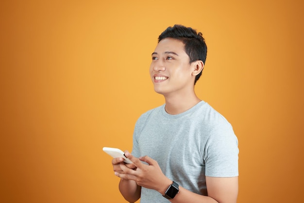 Homme asiatique décontracté intelligent utilisant un smartphone sur fond orange