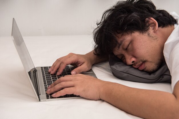 L&#39;homme asiatique dort sur le lit dans la chambre à coucher quitte son travail sur ordinateur.