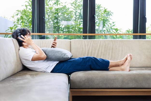 Homme asiatique écoutant de la musique sur un canapé en vacances à la maison Concept de repos et de détente