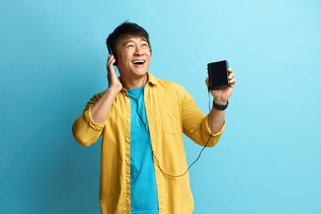 Photo homme asiatique écoutant de la musique homme positif écoutant la radio dans les écouteurs et dansant