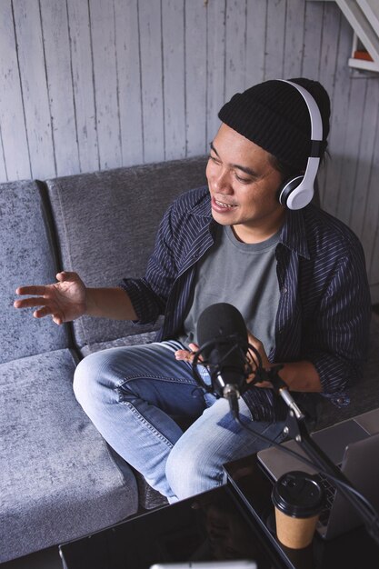 Homme asiatique enregistrant un podcast avec casque et microphone. Podcasteur réalisant des podcasts audio depuis chez lui