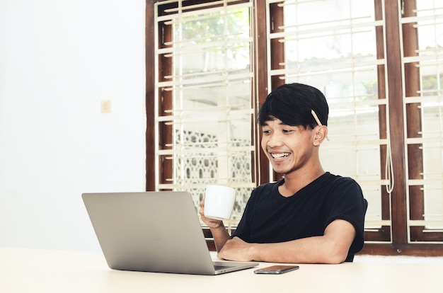 Un homme asiatique est assis devant un ordinateur portable et boit du café