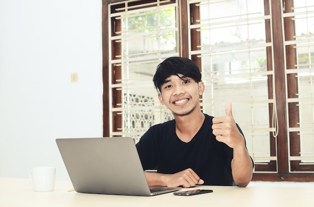 Un homme asiatique est assis devant l'ordinateur portable avec une expression souriante