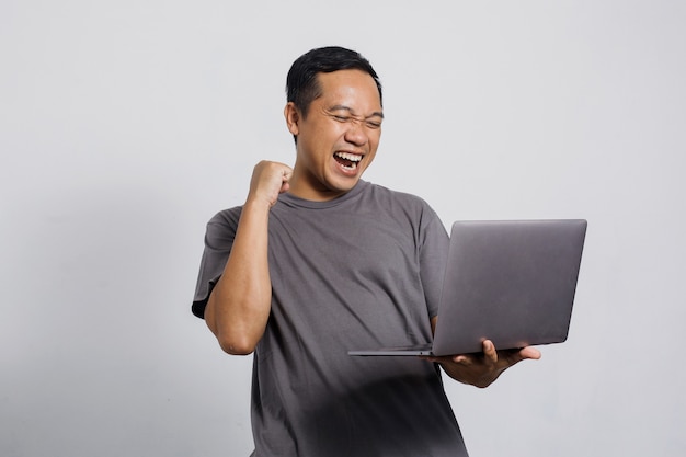 Homme asiatique excité avec un geste gagnant à la recherche d'un ordinateur portable