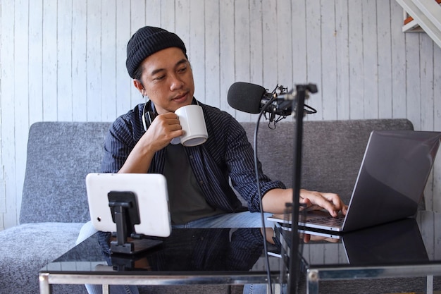 Homme asiatique faisant un podcast à partir d'un home studio tout en tenant une tasse de café. Enregistrement d'un podcast pour o