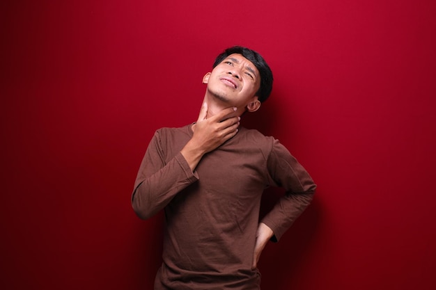 Un homme asiatique sur fond rouge portant un t-shirt marron a mal à la gorge