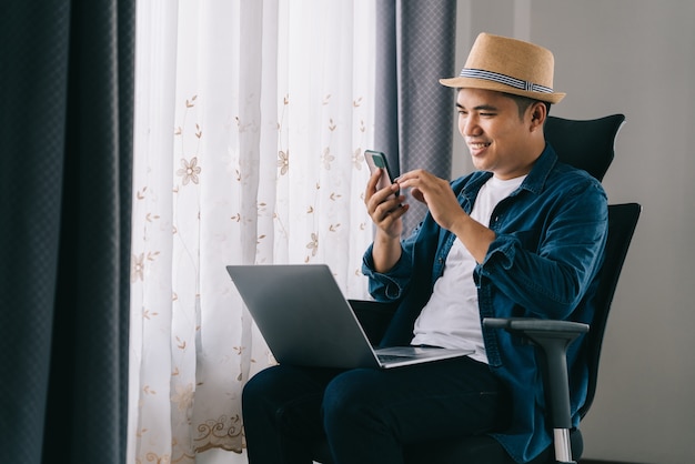 Homme Asiatique Heureux Assis Détendu Et Discuter Avec Les Médias Sociaux Avec Téléphone Mobile, Travail De Concept à Domicile