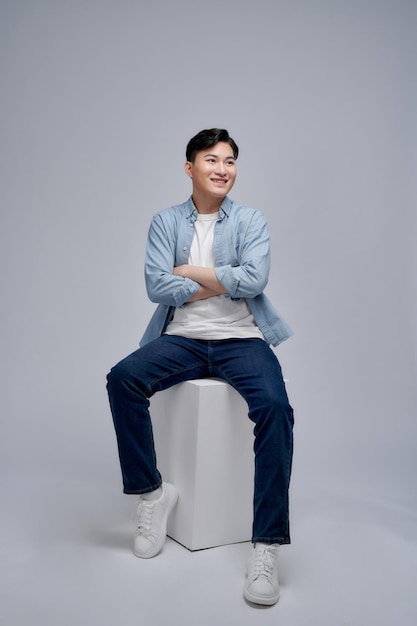 Homme asiatique heureux et confiant se détendre tout en étant assis sur la chaise sur fond blanc