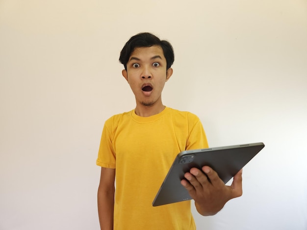 Homme asiatique heureux étonné utilisant une tablette numérique en regardant les nouvelles des médias sociaux homme choqué