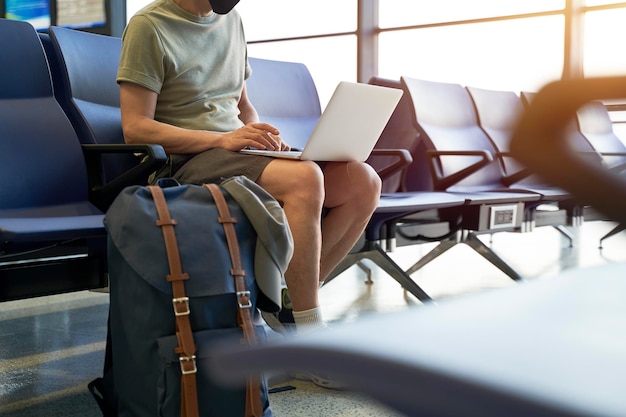 Un homme asiatique, un homme de l'air, assis dans la salle d'attente de l'aéroport en utilisant un ordinateur portable.