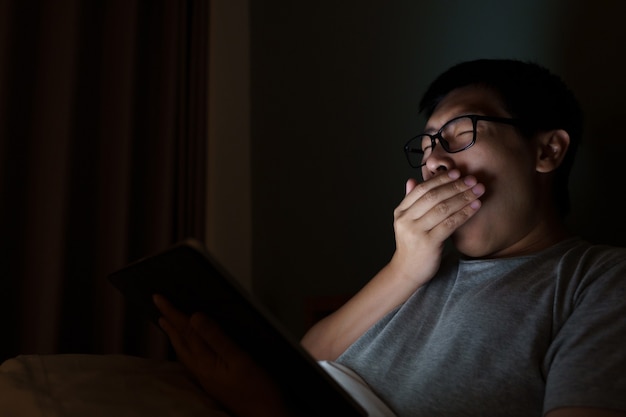 L'homme asiatique joue un ordinateur portable dans son lit. Concept de technologie