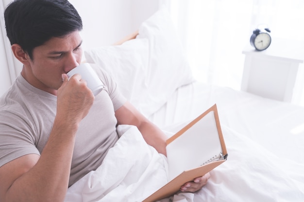 Un homme asiatique lit un livre et boit un café le matin