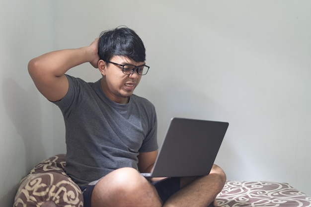 L'homme asiatique à lunettes tient la tête après avoir regardé un ordinateur portable dans une chambre à coucher pour des maux de tête à partir du concept de travail à domicile avec lumière naturelle