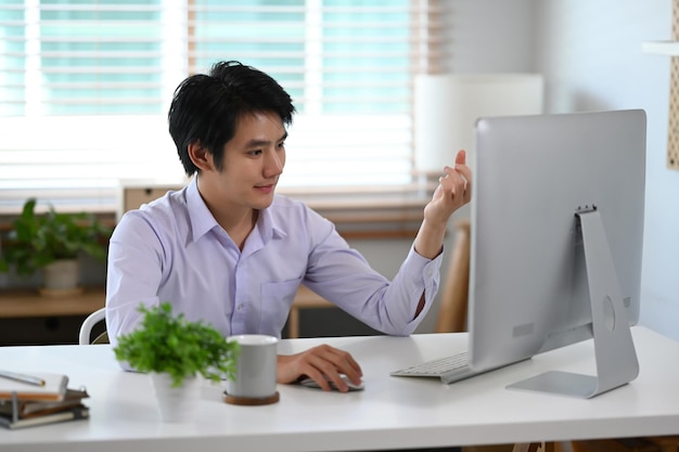 Homme asiatique millénaire souriant travaillant sur un projet dans un bureau à domicile moderne