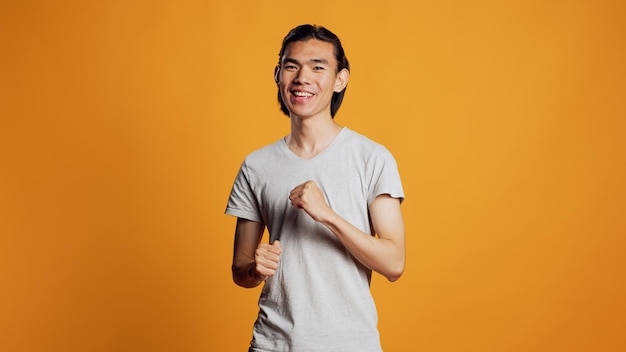 Homme asiatique montrant des mouvements de danse cool devant la caméra, s'amusant à danser avec confiance et style hipster. Jeune mannequin aux expressions amicales agissant groovy et appréciant la musique positive.