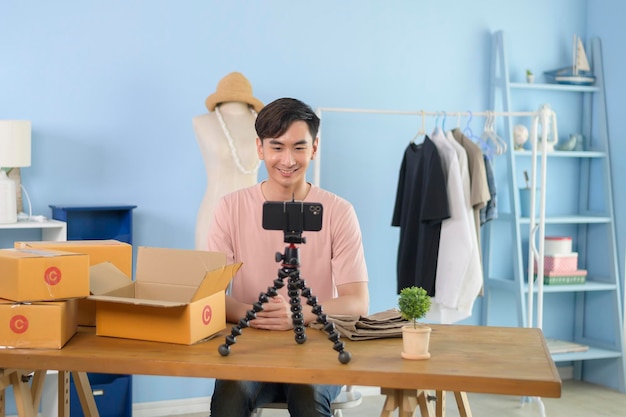 Un homme asiatique montre des vêtements devant la diffusion en direct d'un smartphone dans sa boutique