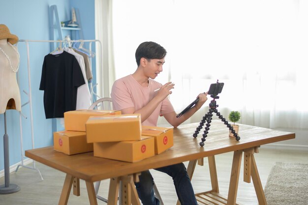 Un homme asiatique montre des vêtements devant la diffusion en direct d'un smartphone dans sa boutique