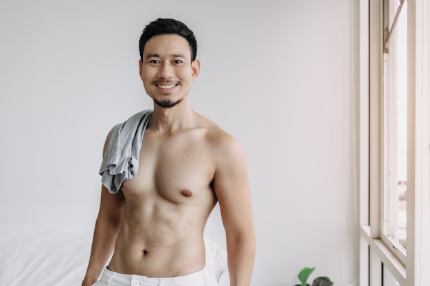 Homme asiatique ne portant pas de haut se détendre après le bain dans le salon de son appartement