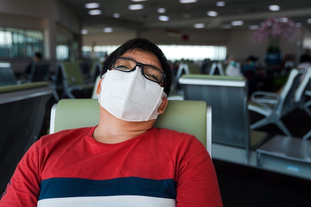 un homme asiatique obèse portant un masque protecteur s'assoit en train de dormir sur un siège de distanciation sociale à l'aéroport