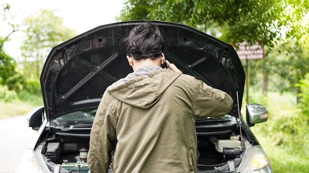 Un homme asiatique a ouvert le capot de la voiture en appelant