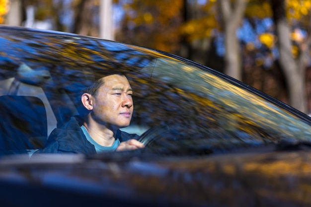Un homme asiatique pensif est assis dans la voiture, le chauffeur attend et est triste