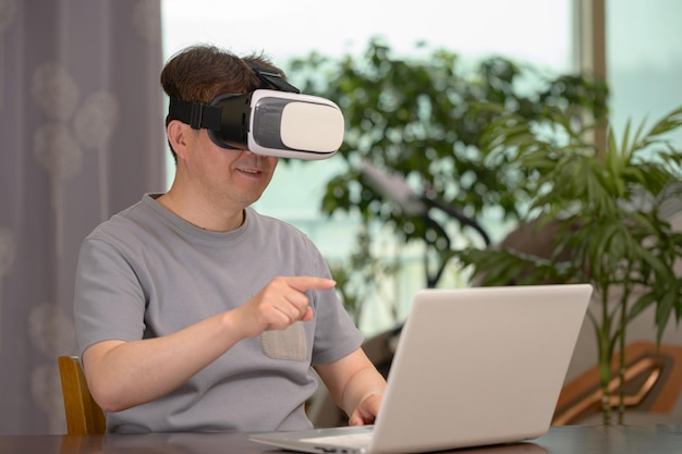 Photo homme asiatique portant un casque vr et utilisant un ordinateur portable assis à son bureau