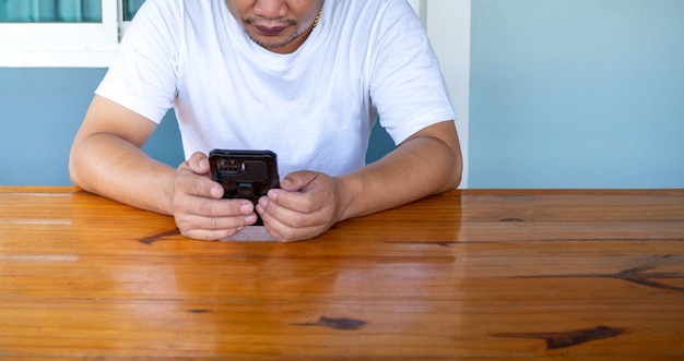 Homme asiatique portant une chemise blanche à l'aide du téléphone sur une table en bois