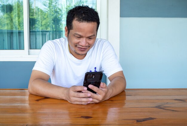 Homme asiatique portant une chemise blanche à l'aide du téléphone sur une table en bois