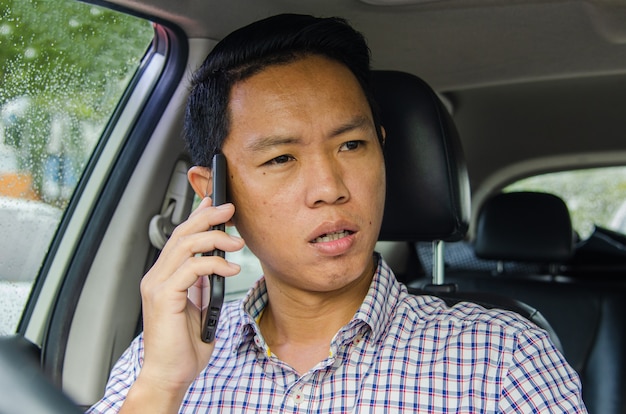 Homme asiatique portant une chemise à carreaux se penche sur un téléphone intelligent dans une voiture.