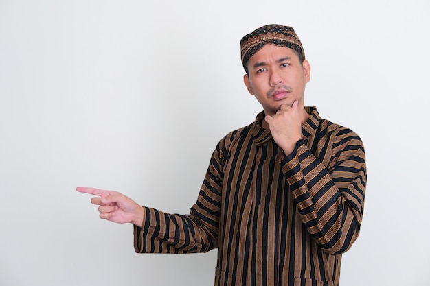 Homme asiatique portant un costume traditionnel javanais pointant vers le côté droit avec une expression de pensée