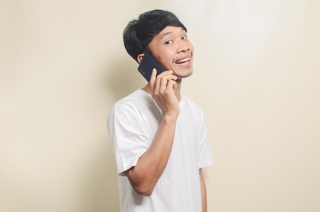 Homme asiatique portant un t-shirt blanc brillant avec un geste heureux tout en appelant son ami sur fond isolé